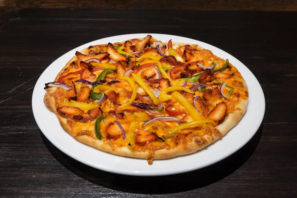 Round pizza with chicken, melted cheese, bell peppers, and onions.