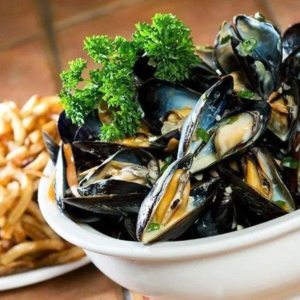 White bowl of steamed mussels with parsley and french fries.