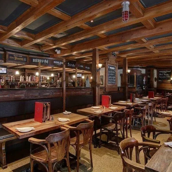 Rustic French restaurant interior with dark wood paneling and a bar.