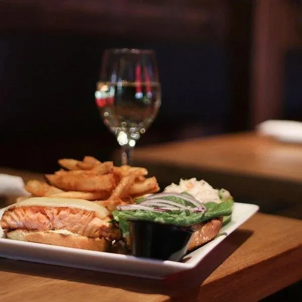 Grilled salmon sandwich, thick fries, side salad, and a wine glass.