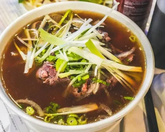 Close-up of hot pho soup with beef, onions, and scallions.