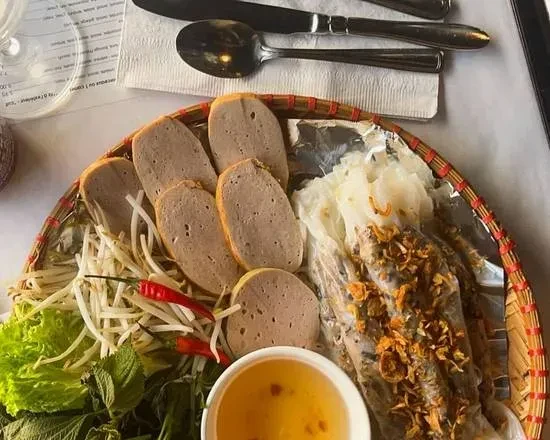 Overhead view of Vietnamese rolled rice sheets with ham, herbs, and sauce.