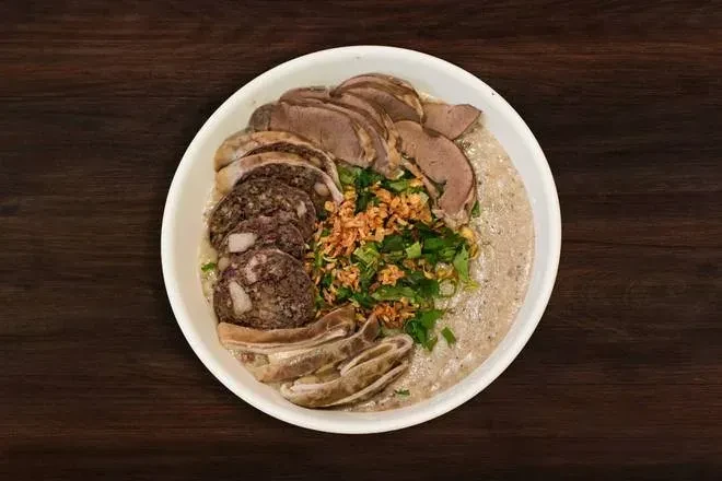 Top-down bowl of creamy savory food with meats, herbs, fried shallots.