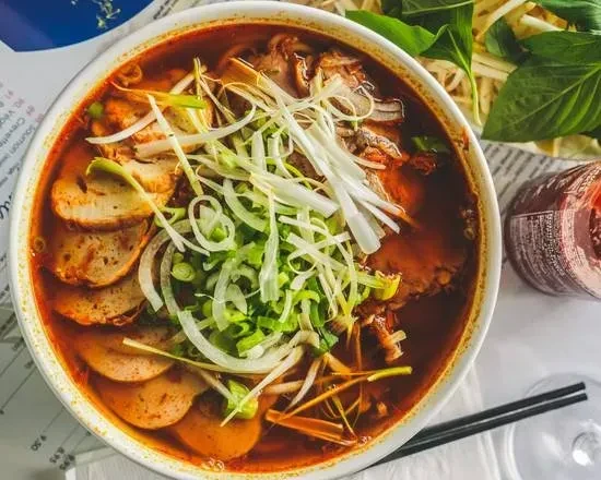 Overhead close-up of Vietnamese noodle soup with meat, onions, and herbs.