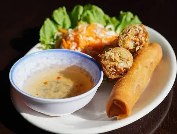 Close-up of crispy Vietnamese spring rolls with dipping sauce and salad.