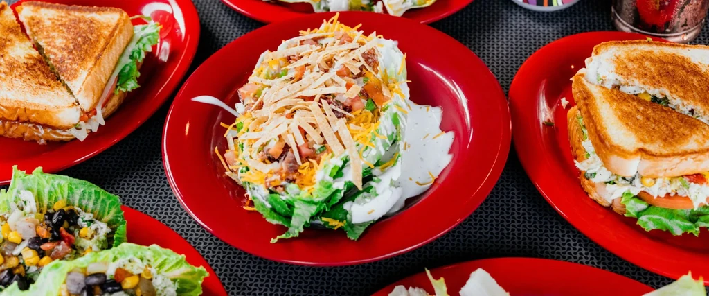 Colorful taco salad, grilled sandwiches, and lettuce wraps on red plates.