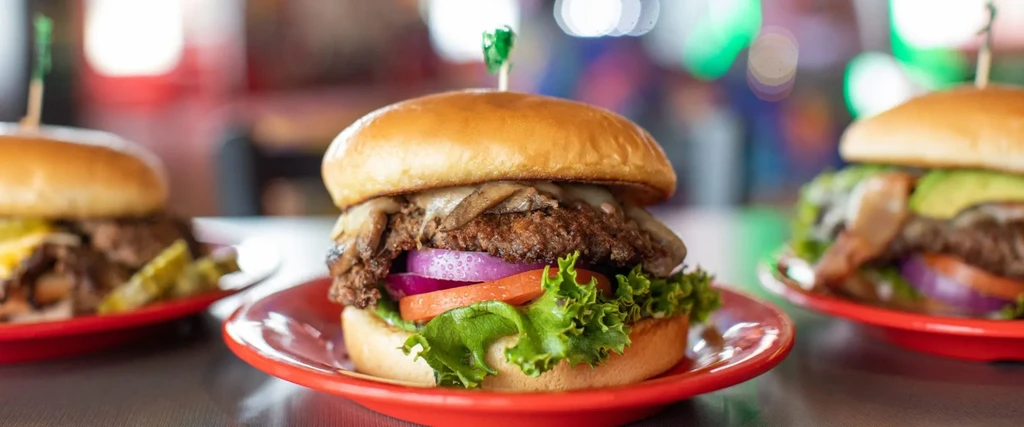 Three gourmet burgers on red plates; central one with mushrooms in focus.