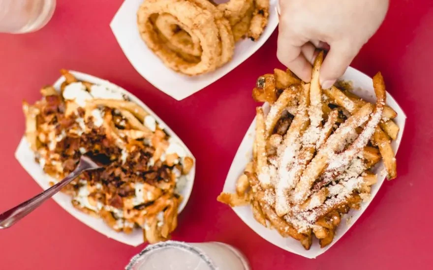 A hand picks a fry from parmesan, loaded fries, and onion rings.