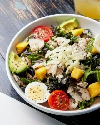 Colorful chicken salad with avocado, mango, cheese, and egg on wood.