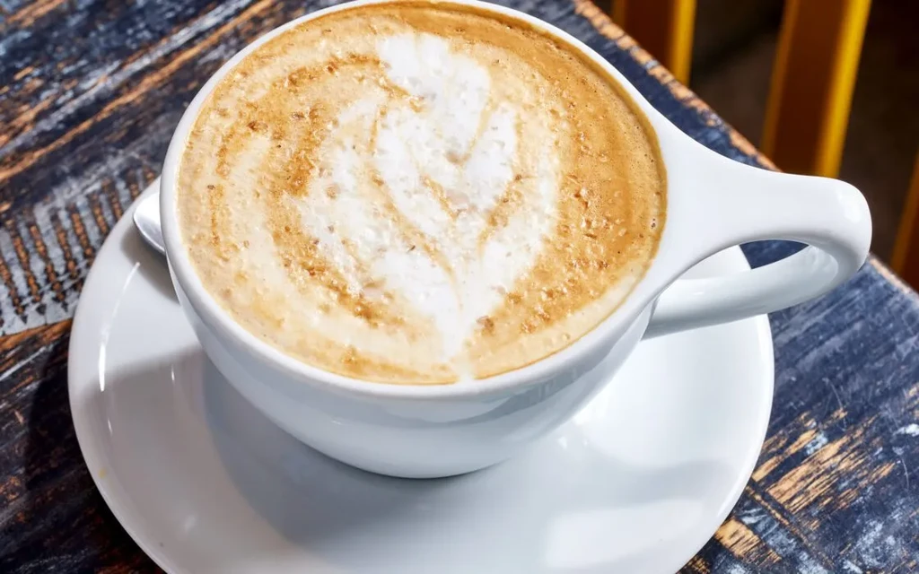 Close-up of latte with latte art in white cup on wooden table.