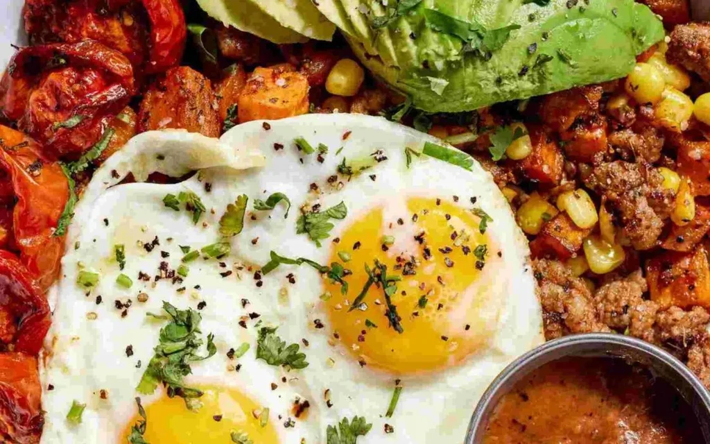 Breakfast bowl with two fried eggs, ground meat, avocado, and vegetables.