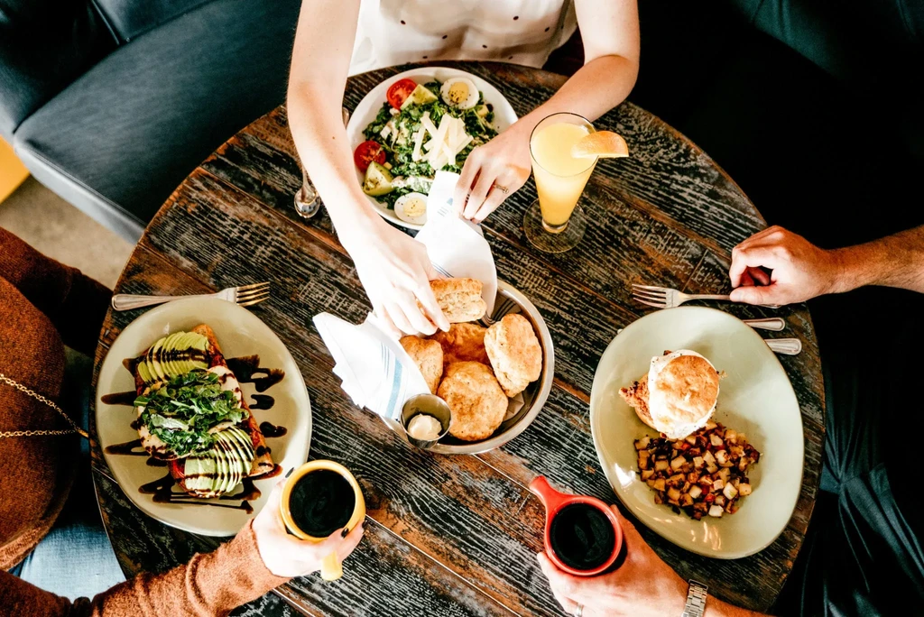 Overhead of brunch dishes on a rustic wooden table with four hands.