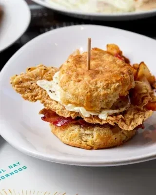 Biscuit sandwich with crispy fried chicken, fried egg, bacon, and potato wedges.