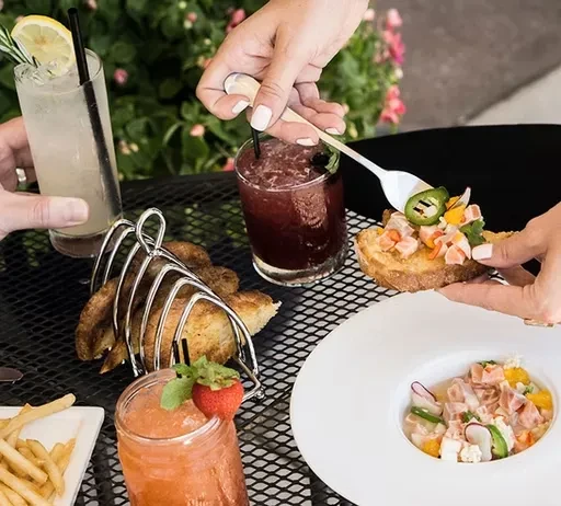 Hands interacting with a variety of food and drinks outdoors.