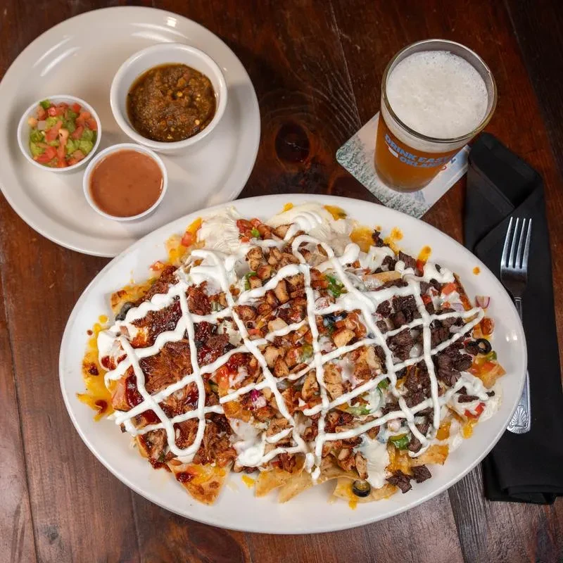 Heavily loaded nachos with three meats, toppings, dips, and a beer.