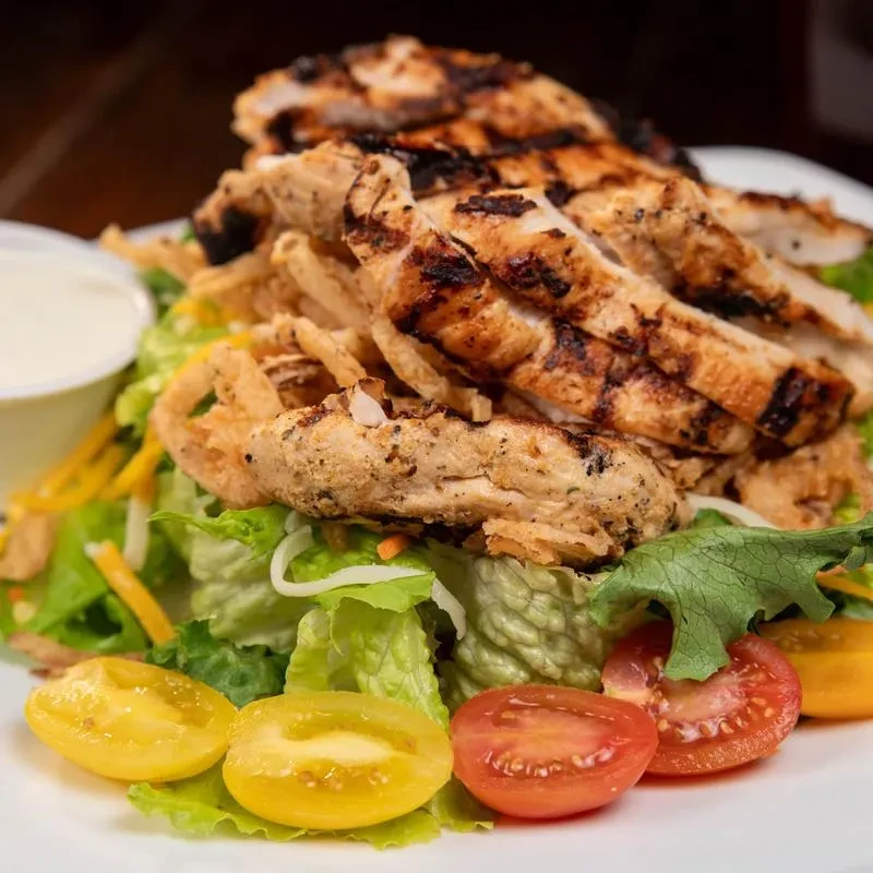 Grilled chicken salad with lettuce, colorful tomatoes, and crispy fried elements.