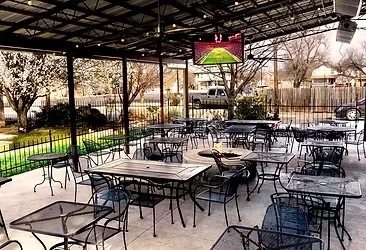 Empty covered restaurant patio with fire pit, sports TV, and bare trees.