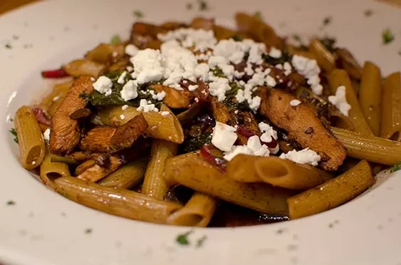 Penne pasta with chicken, vegetables, reddish sauce, crumbled cheese, herbs.
