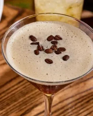 Top-down: Dark cocktail in martini glass, foam, and coffee bean garnish.