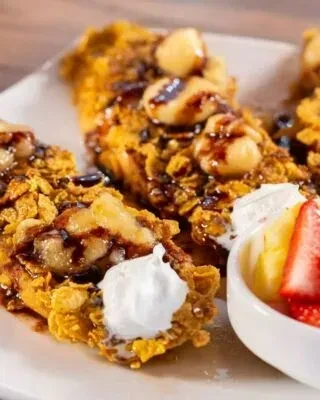 Crunchy French toast with bananas, macadamia nuts, syrup, whipped cream, and fruit.