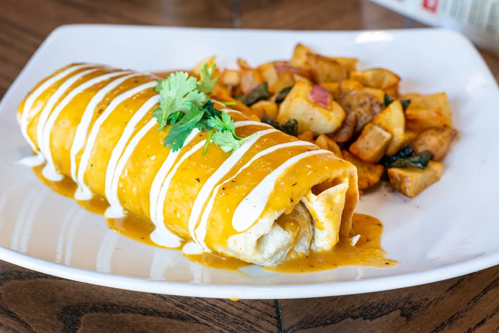 Close-up: Sauced breakfast burrito with crema, cilantro, and crispy home fries.