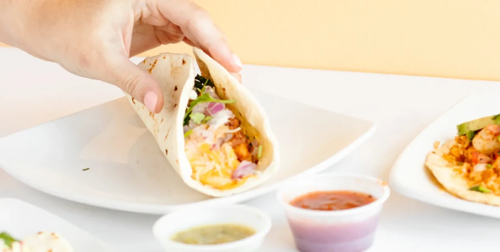 Hand holding a taco with meat, cheese, onions, and cilantro.
