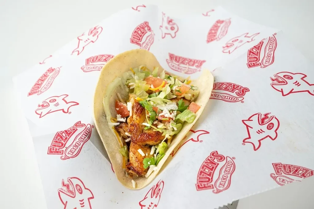 A chicken taco rests on Fuzzy's Taco Shop branded parchment paper.