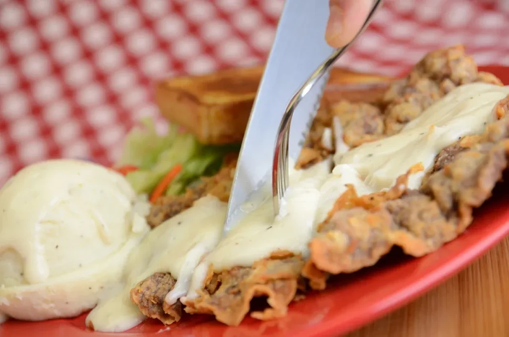 Hand cutting gravy-covered fried steak and mashed potatoes.