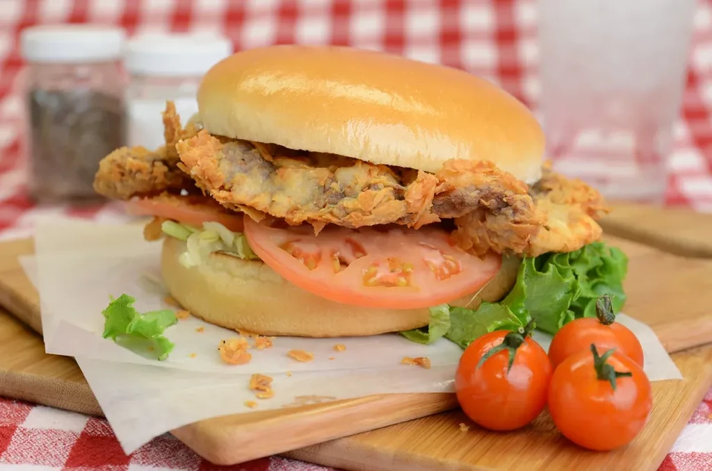 Crispy fried fish sandwich, lettuce, tomato, cherry tomatoes on wooden board.