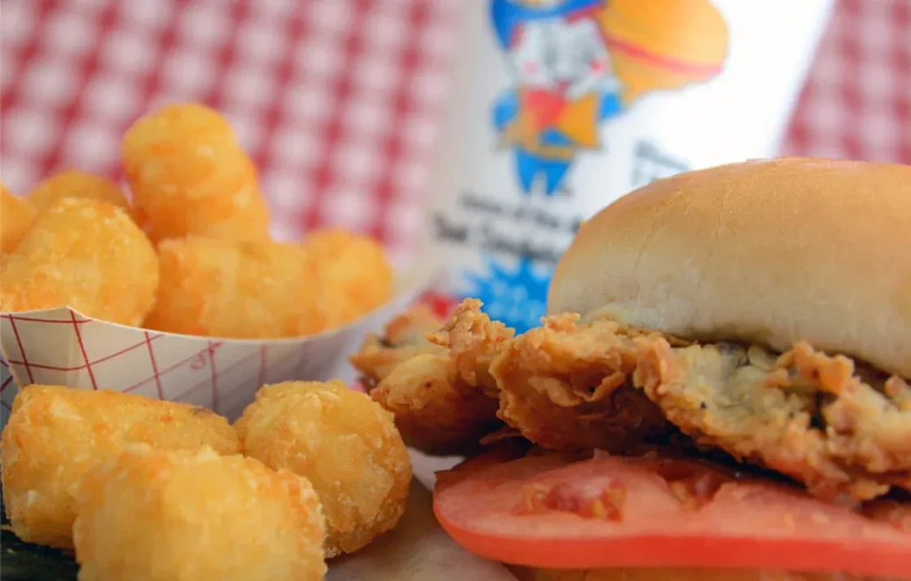 Tater tots and a fried chicken sandwich on a red and white tablecloth.