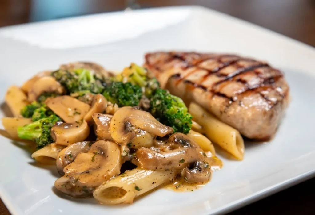 Grilled meat, penne pasta with mushrooms, broccoli, and creamy sauce.