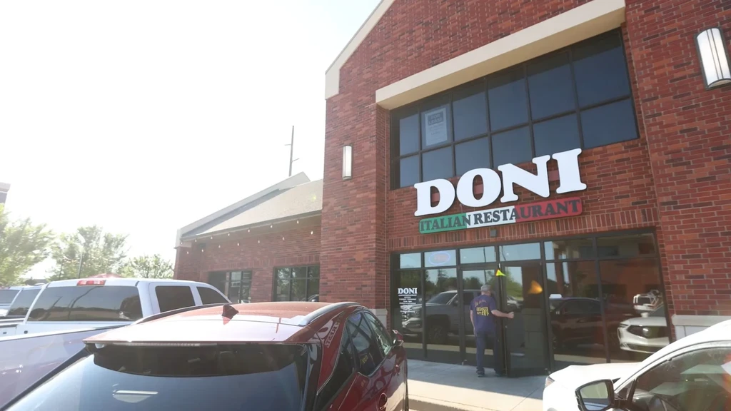 Red brick Doni Italian Restaurant building, parking lot with cars, person entering.