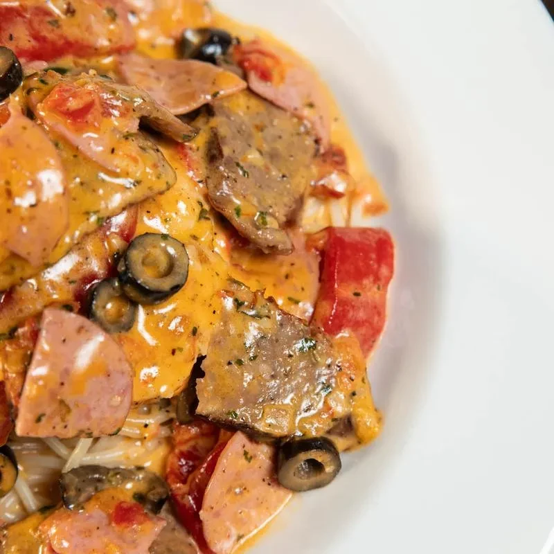 Close-up of creamy pasta dish with meats, olives, and red vegetables.