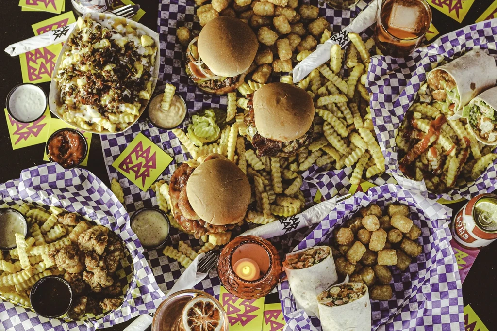 Overhead shot: burgers, fries, chicken, and drinks with purple checkered paper.