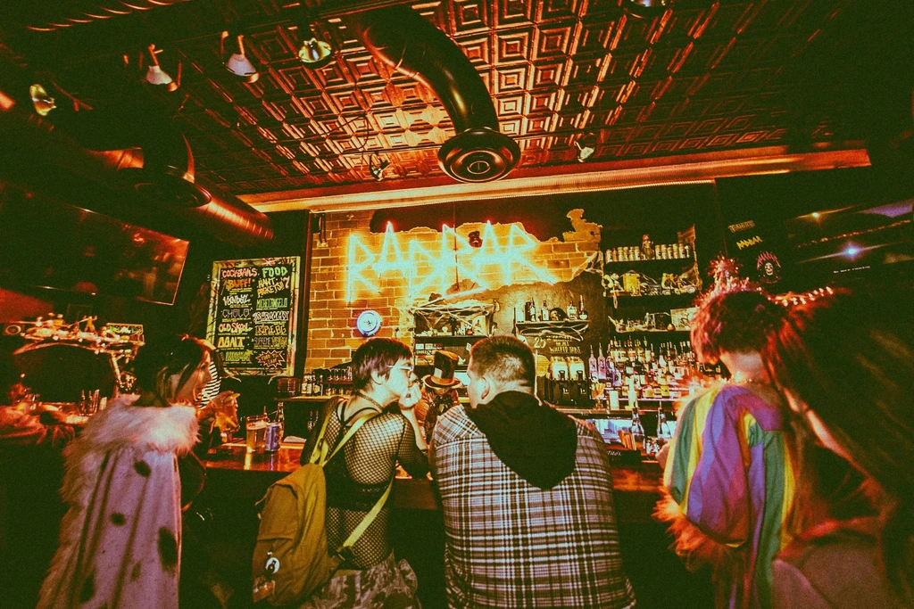Retro-filtered bar interior with 'RADAR' neon sign and seated patrons.