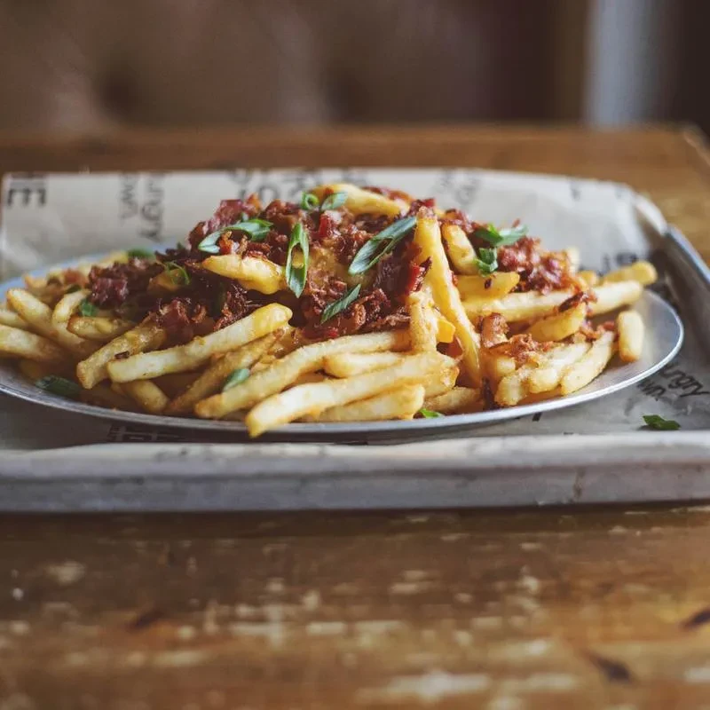 Close-up of golden loaded French fries with meat, sauce, and green onions.