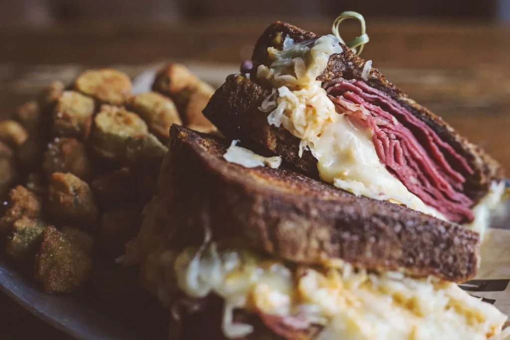 Stacked deli sandwich with thick meat, melted cheese, sauerkraut, rye bread.