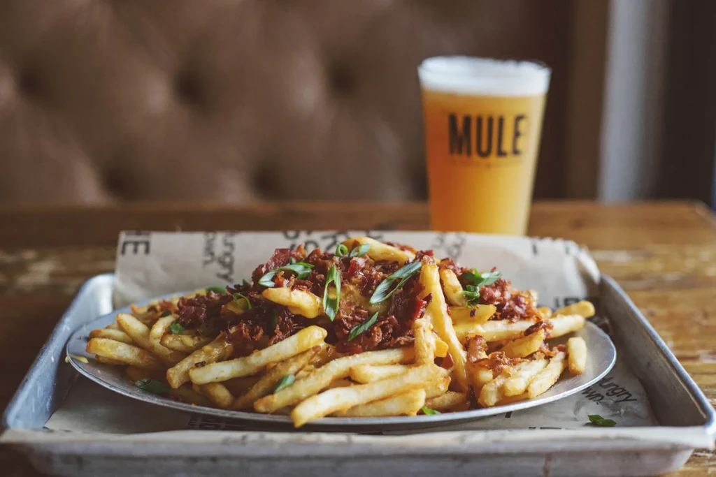Loaded fries with bacon, cheese, and green onions; beer in background.