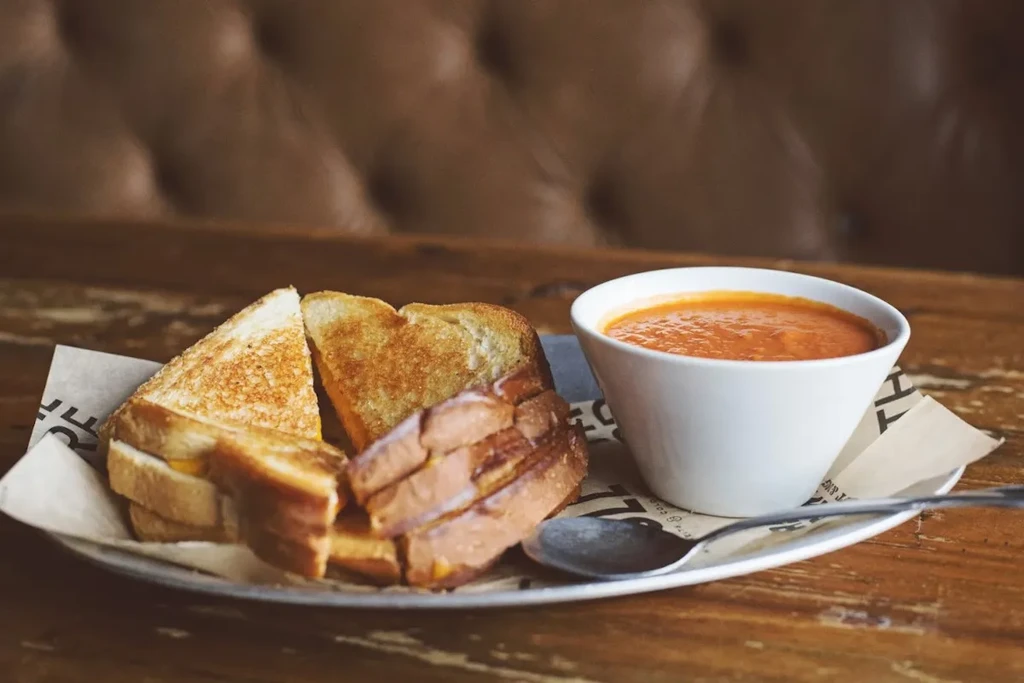 Golden grilled cheese, tomato soup, and spoon on a rustic table.