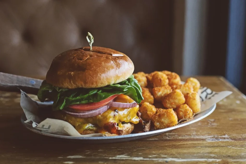 Tall burger with melted cheese, fresh toppings, and crispy tater tots.