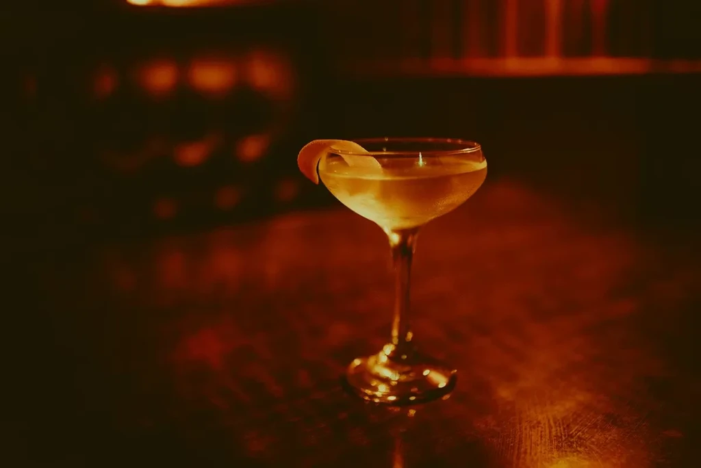 Golden cocktail in a coupe glass with a curled citrus peel.