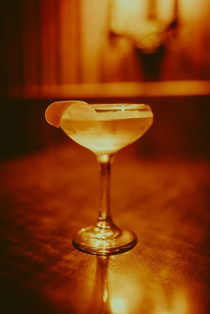 Warmly lit clear cocktail in a coupe glass with lemon peel.