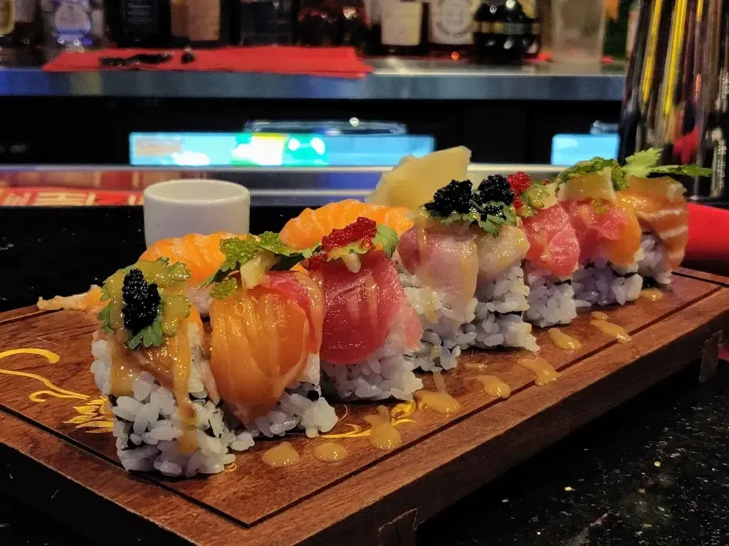 Artistic sushi platter with fish, caviar, sauce, on a dark board.