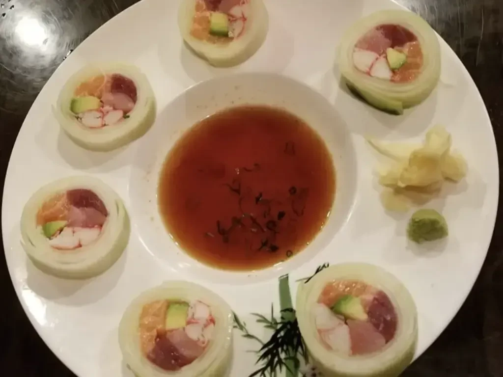 Top-down view of naruto sushi rolls with salmon, tuna, sauce, and sides.