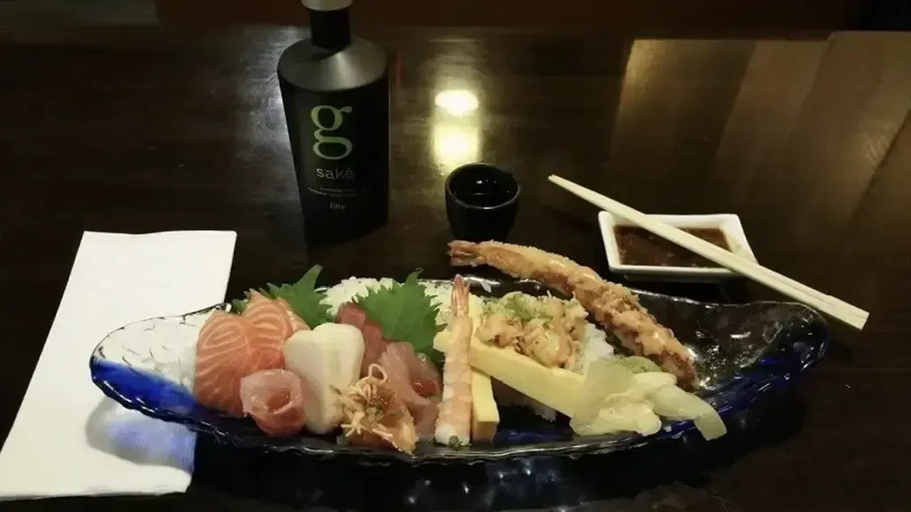 Japanese sushi and sashimi platter with sake bottle on wooden table.