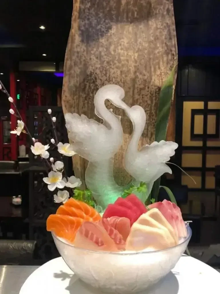 Sashimi in glass bowl, an ice sculpture of swans, and blossoms.