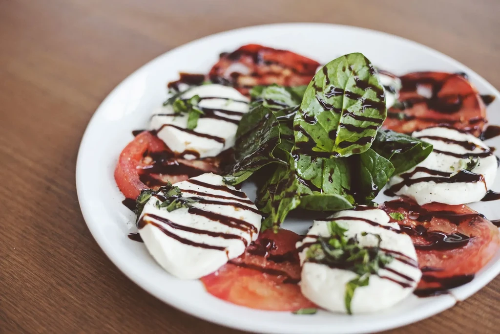 White plate with sliced tomatoes, mozzarella, basil, and balsamic glaze.