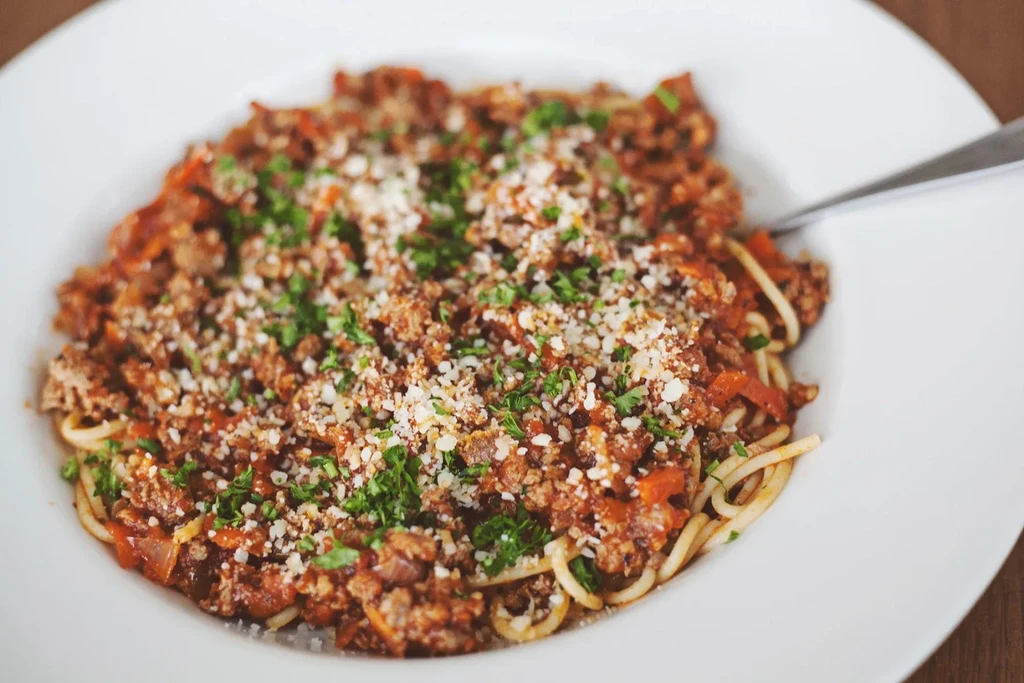 Close-up of spaghetti bolognese with Parmesan, herbs, and a fork.
