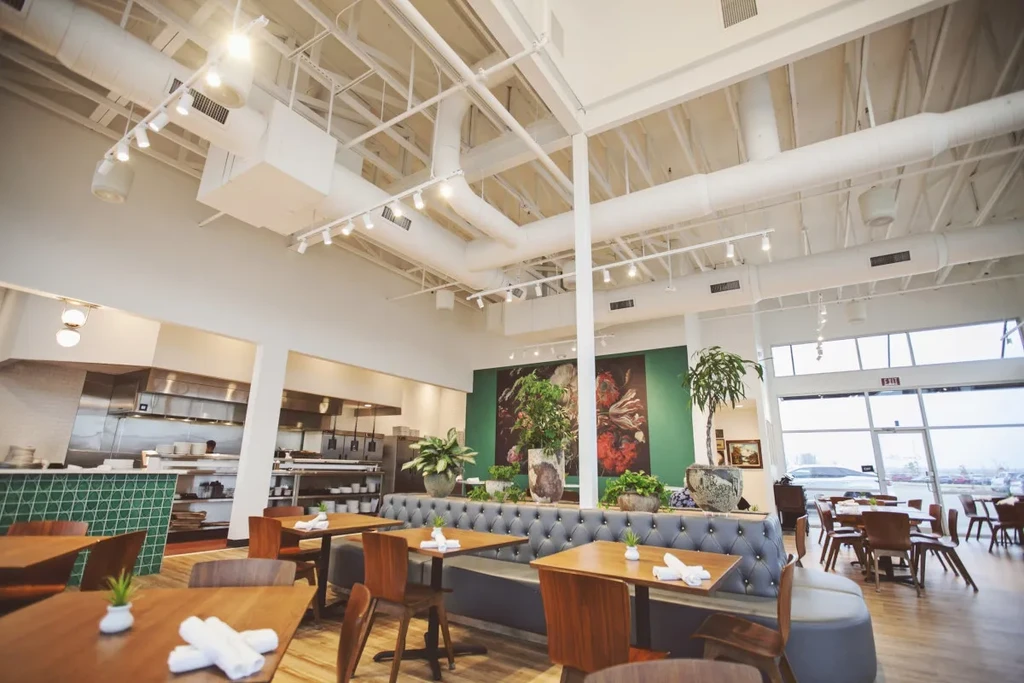 Bright, contemporary restaurant with open kitchen, green botanical art, and plants.