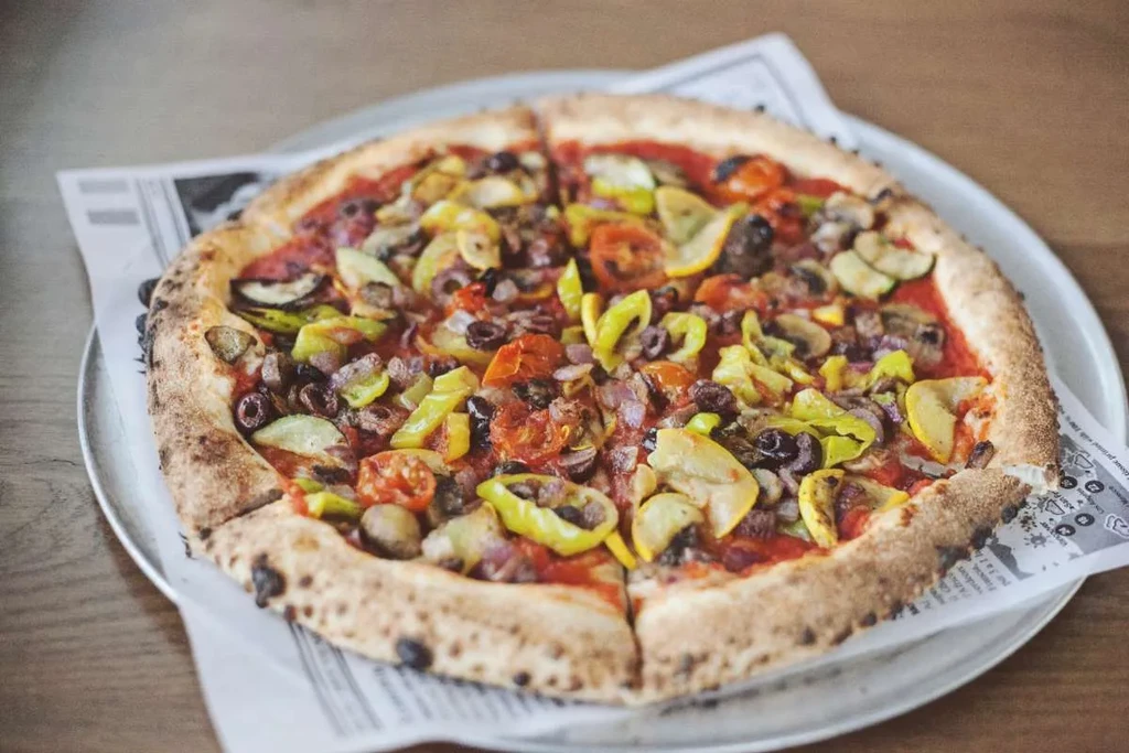 Sliced, wood-fired vegetable pizza on a silver tray.